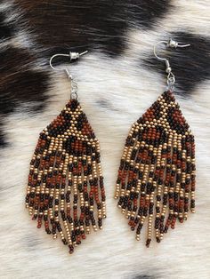 two pairs of beaded earrings on top of a cowhide fur background, one with brown beads and the other with white beads