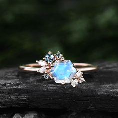 an engagement ring with blue and white stones on top of a piece of drift wood