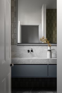 a bathroom sink sitting under a large mirror next to a white door with a vase on it