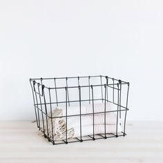 a black wire basket with folded towels in it on a wooden table next to a white wall