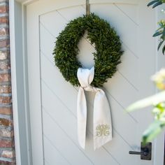 a wreath is hung on the front door with two white napkins tied to it