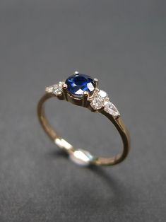 a gold ring with two diamonds and a blue sapphire stone on the side, sitting on a gray surface