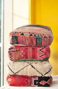 a stack of colorful pillows sitting on top of a bed next to a yellow wall