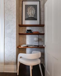 a white chair sitting in front of a wooden shelf filled with books and art on top of it