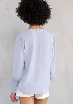 Designed in ultra-soft and silky crepe, this effortless bohemian peasant top is an instant classic. Featuring a delicate self-covered button front detail, voluminous long sleeves with a smocked elastic wrist cuff, and smocking along the shoulder. Try this versatile style tucked into trousers or untucked over jeans. Silky crepe Relaxed fit Long voluminous sleeve Smocked elastic wrist cuff Split v-neckline with ties Ruffled neckline Self-covered button front Smocked shoulder details Bohemian resor Billowy Long Sleeve Top With Smocked Cuffs, Billowy Long Sleeve Top With Gathered Sleeves, Flowy Puff Sleeve Tops With Elastic Sleeves, Fall Peasant Top With Blouson Sleeves For Daywear, Feminine Tops With Smocked Bishop Sleeves, Long Sleeve Smocked Top For Daywear In Spring, Long Sleeve Smocked Top For Spring Daywear, Long Sleeve Tops With Elastic Sleeves For Daywear, Flowy Smock Blouse