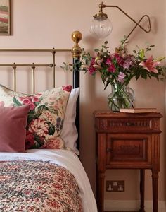 a bed with pink and green flowers on it next to a night stand that has a lamp