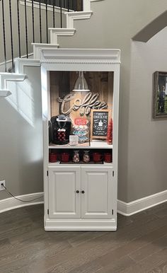 a white cabinet sitting in the middle of a living room next to a stair case