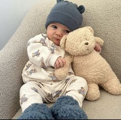 a baby sitting on a couch with a teddy bear in his lap and wearing a hat