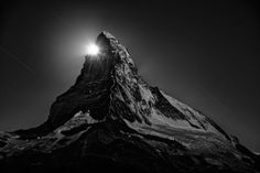 the top of a mountain is lit up at night with stars in the sky above it