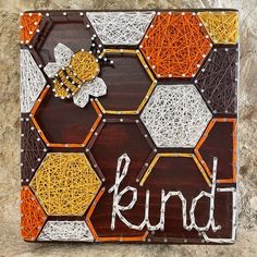 the word kind written in white and orange yarn on a wooden board with hexagons