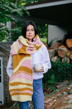 a woman wearing a striped scarf and holding a coffee cup in her hand while standing outside