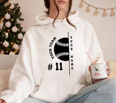 a woman sitting on a couch holding a coffee cup and wearing a baseball hoodie