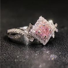 a pink diamond ring sitting on top of a black surface with white diamonds around it