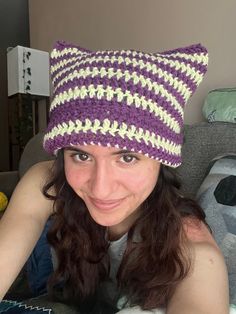 a woman laying on top of a couch wearing a purple and white knitted cat hat