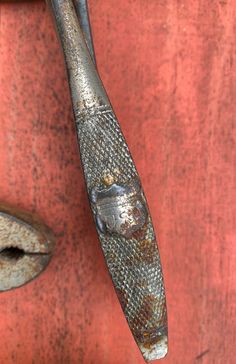 an old metal object hanging on the side of a red wall with rusted paint