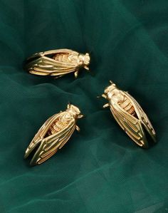 three gold bee brooches sitting on top of a green cloth