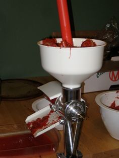 a blender filled with red liquid sitting on top of a wooden table next to a bowl