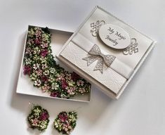 a box with some flowers in it on a white table next to a pair of earrings