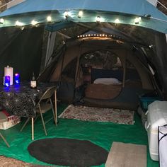 a tent is set up in the woods with lights strung from it's ceiling