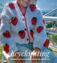 a woman sitting on top of a chair wearing a white sweater with strawberries on it