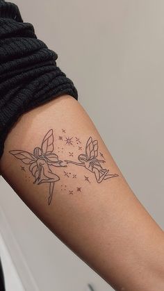 a woman's arm with a tattoo on it that has flowers and two fairy wands