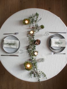 the table is set with silverware, candles and greenery