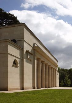 an old building with columns and a clock on the front wall is shown against a cloudy sky