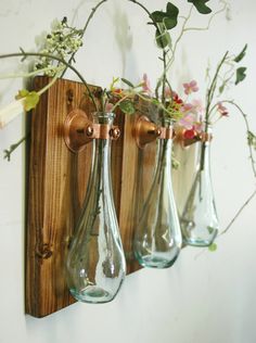 three glass vases with flowers in them hanging on a wooden wall mounted hook up to a white wall