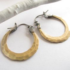 "Small handcrafted forged bronze hoops with sterling silver ear wires. Artfully hammered for dynamic texture and fitted with 20 gauge ( standard size) sterling silver ear wires with a secure and easy to use friction clasp. Lightweight at less than 4 grams each.A perfect pair for any time, anywhere! 1 and 1/8\" wide or 2.66cm and apx. 1.25\" tall or 3.1cm. If you would prefer a slighter thicker (18 gauge) ear wire please let us know in notes to seller at the time of purchase. The pair pictured ha Metalsmith Jewelry, Metalsmithing Jewelry, Mixed Metal Earrings, Hammered Hoop Earrings, Bronze Earrings, Hammered Earrings, Ear Gauges, Metal Earrings, Brass Earrings