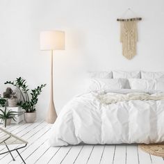 a bedroom with white bedding and plants on the floor, along with a lamp