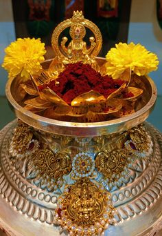 a metal bowl filled with red and yellow flowers on top of a silver plate covered in gold