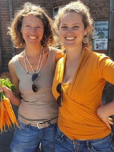 two women standing next to each other holding carrots