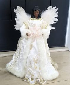 a doll dressed in white and gold with angel wings on it's back, standing next to a door