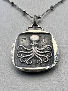 an octopus pendant is shown on a silver plated chain, with the word's symbol