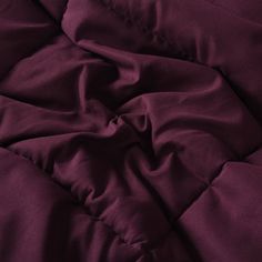 an unmade bed with purple sheets and pillows