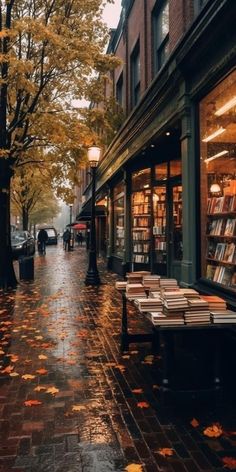 an empty sidewalk in front of a book store with autumn leaves on the ground and people walking by