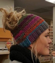 a woman with her hair in a messy ponytail wearing a multicolored knitted hat