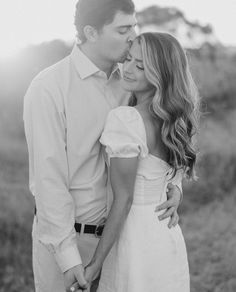 a man and woman kissing each other in a field with the sun shining down on them