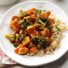 a white plate topped with chicken and broccoli covered in sauce next to rice