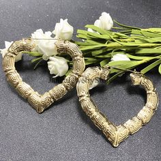 two gold heart shaped frames sitting next to flowers on a black surface with white tulips in the background