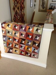 a very colorful quilt sitting on top of a white shelf next to a chair and rug