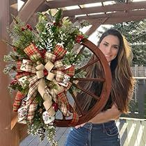 a woman holding a christmas wreath on top of a wooden wheel