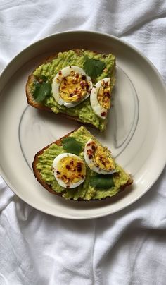 two pieces of toast with eggs on top and avocado in the middle sitting on a white plate