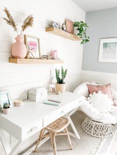 a white desk with some plants and pictures on the wall above it in a room