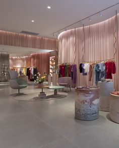 the inside of a clothing store with clothes on racks and tables in front of it