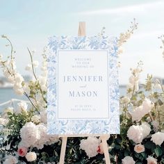 a welcome sign sitting on top of a wooden easel next to flowers and water