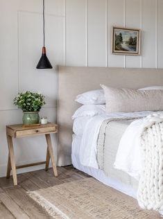 a bed with white linens and pillows in a bedroom next to a wooden table