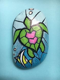 a painted rock with a flower and fish in it on a blue tablecloth background