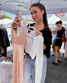 a woman is looking at clothes hanging on a rack in an outdoor market area with people standing around