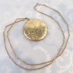 An elaborate engraved foliate design tops this large 1 5/8-inch round Antique gold filled locket. The design was finely carved with flowers, leaves, scrolled lines, a fine straight line sun ray pattern and has a blank area meant for a monogram. The back has a plain shiny gold finish.  The locket opens with a small fingernail groove at the top and closes lightly, but securely. The inside has no frames or inserts, just an old black and white photograph. One side is signed, "D&C" and the locket tested as gold filled (no hallmark). The large pendant hangs from a thick, well-made sturdy vintage gold filled curb chain. It has a nice sheen and true vintage look. The chain stretches 23 1/2 inches and has no clasp. It must be put over the head to wear, so it may not fit everyone. This pairing is in Gold Medallion Locket Necklace Stamped 14k, Gold Medallion Locket Necklace In Brass, Antique Medallion Necklace With Locket, Victorian Round Locket Necklace Stamped 14k, Antique Medallion Locket Necklace Stamped 14k, Ornate Gold Locket Necklace In Brass, Ornate Gold Brass Locket Necklace, Ornate Engraved Medallion Locket Necklace, Antique Medallion Locket Necklace